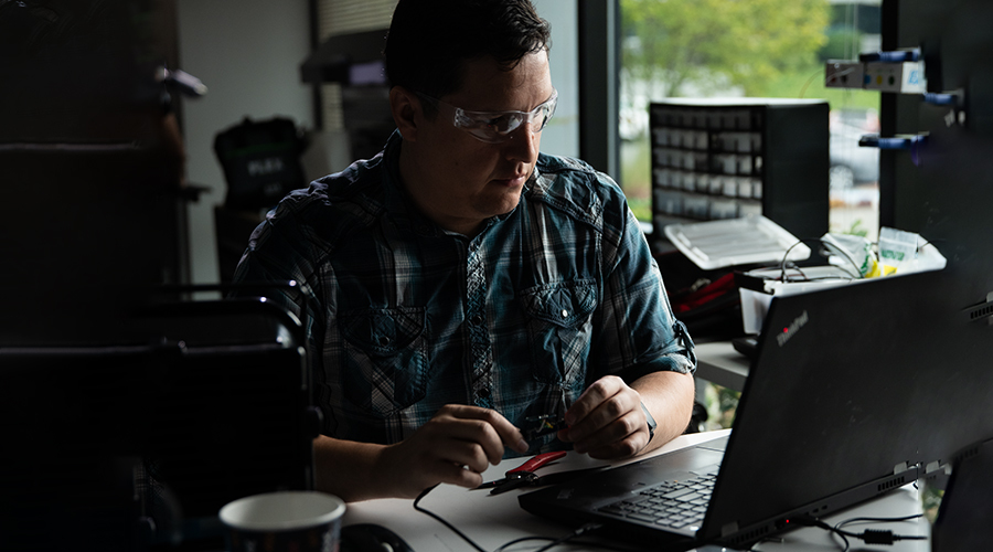 Male Lowe's Innovation Labs team member working on laptop and checking circuitry. 